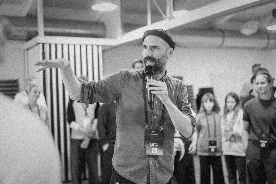 Lutz Woellert mitten in einer Workshop-Gruppe, mit erhobener Hand im Gespräch
